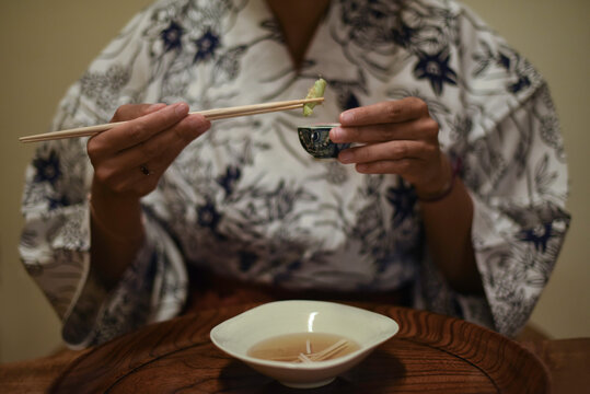 Close up view of hands of female caucasian woman in kimono using chopsticks to eat Japanese food at ryokan