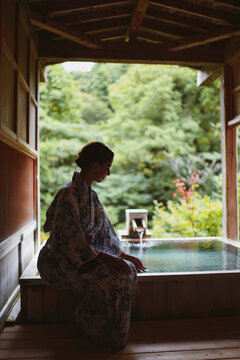 Young caucasian woman in a kimono touching thermal waters before enjoying a traditional bath at a Japanese onsen
