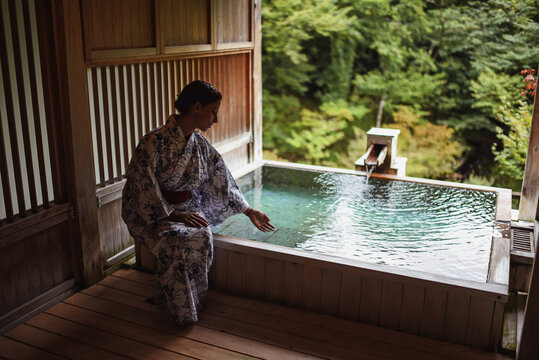 Young caucasian woman in a kimono touching thermal waters before enjoying a traditional bath at a Japanese onsen