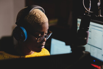 Side view of african American female radio host working in dark broadcast studio and speaking in microphone