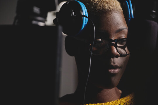 Cheerful black woman in headphones working in broadcast station and speaking in modem microphone