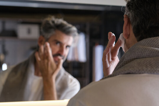 Stock photo of middle aged man with grey hair preparing for shaving his beard in the bathroom.