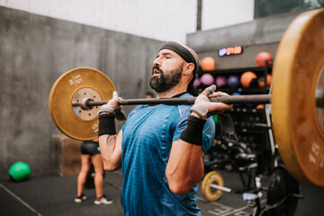 Side view of muscular male athlete doing clean and jerk exercise while training in modern fitness center