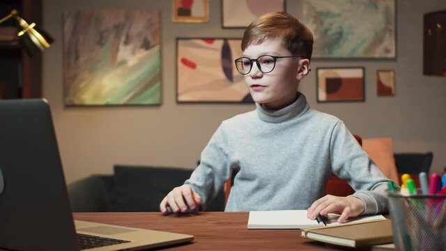 Boy kid making video call with laptop at home, using camera zoom online virtual class, social distancing, learning remotely at school during covid coronavirus lockdown