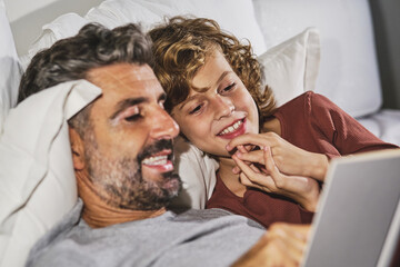 Close up view of peaceful man and boy lying on bed and reading interesting story in book together