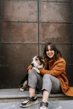 Side view of female owner gently embracing Treeing Walker Coonhound dog while sitting on street in city