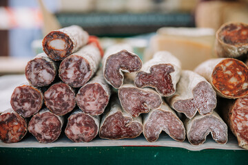Various types of delicious spicy aromatic cured meat sausages stacked on counter of local farmers market