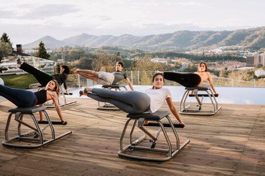 Company of people in sportswear doing abs exercises on pilates chair during training on terrace on sunny day