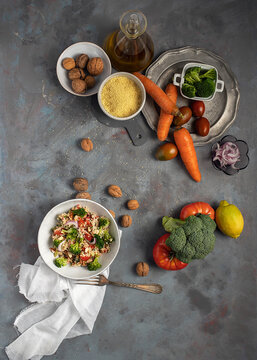 Top view of bowl with healthy homemade bulgur couscous salad with various vegetables and walnuts served on table with ingredients