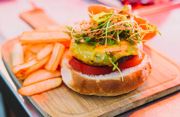 Hamburquesa con queso tomate y rúcula acompañada de patatas fritas.