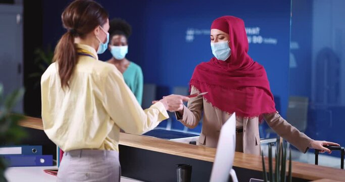 Security Agent Woman Wearing Surgical Mask Servicing Multi-National Customers in Airport Terminal. Check-In Flight. Registration Counter. Quarantine.