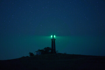 Beacon tower located on hill and illuminating darkness with green light on background of starry night sky