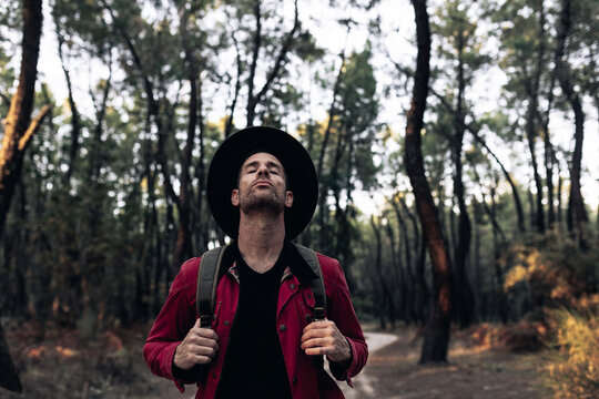 Adult traveler in hat closing eyes and breathing peacefully in harmony with nature of forest