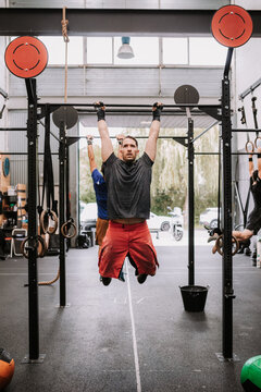 Determined male athlete making effort and pulling up on bar during active workout in gym