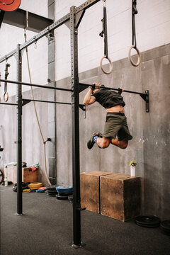 Determined male athlete making effort and pulling up on bar during active workout in gym