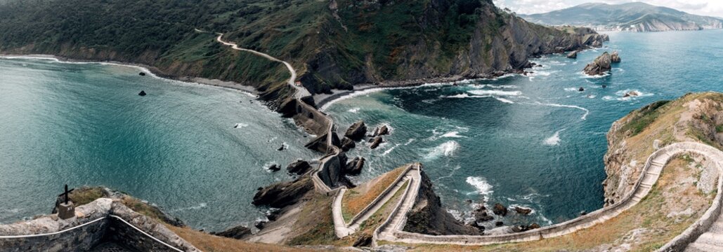 From above of constructed narrow walkway on mountains separating ocean with waves forming foam under cloudy sky