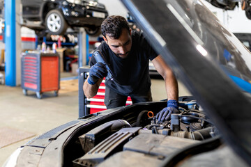 Serious male mechanic with flashlight examining lifted car while working in automobile service
