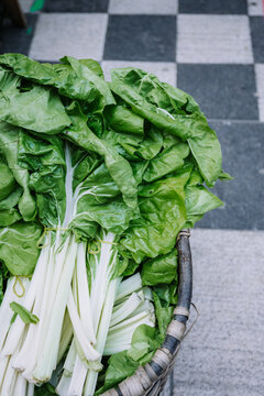 Top View Of Basket With Heap Of Fresh Organic Green Chard Placed On Stony Ground On Agricultural Market