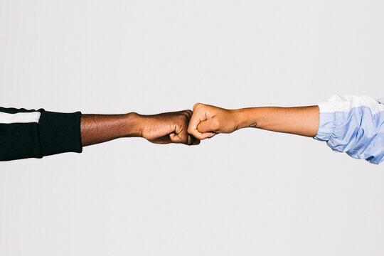 Close-up Of A Man's Black Fist Bumping Into A White Woman's Fist Over White Background