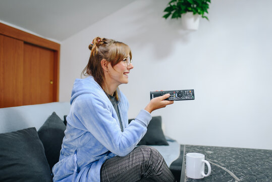 Girl sitting on a sofa in a robe and using a remote control television