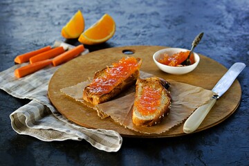 Open sandwiches or toasts on white bread with carrot jam on a wooden board on a black concrete background. Vegetable jams.