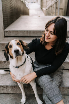 Side view of female owner gently embracing Treeing Walker Coonhound dog while sitting on street in city