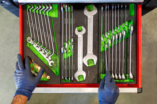 Top view of crop unrecognizable male technician standing near tool cabinet with collection of various spanners in car service