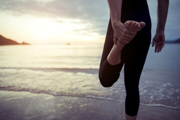 Back view of crop anonymous male swimmer in swimsuit stretching body while balancing on leg on wet beach near sea and preparing for swimming