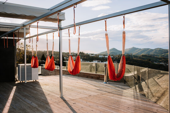 Vivid orange hammocks for yoga hanging on metal bars above terrace on sunny day