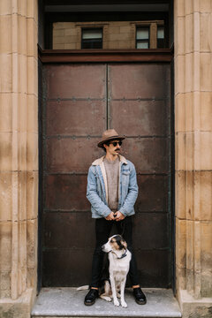 Male in trendy outfit standing near doors in city with Treeing Walker Coonhound dog on leash during city stroll