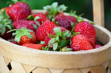 Ripe strawberries with leaves in wicker basket on wooden table on blurred background