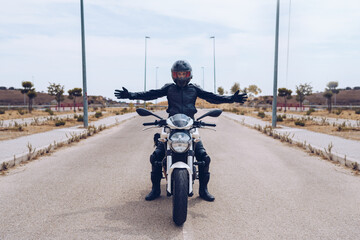 Full body of unrecognizable motorcyclist in black outfit and helmet sitting on modern motorbike parked on roadway