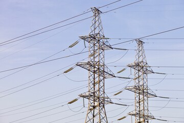 High voltage power lines pylons and electrical cables on a clear blue sky background. Modern infrastructure of high voltage transmission lines. Overhead power lines towers equipment. Energy industry.