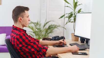 Side view, graphic designer guy using pen tablet does retouching in front computer at home. photographer processes photos. blank white computer screen. Freelancer. Remote work. Retouching training