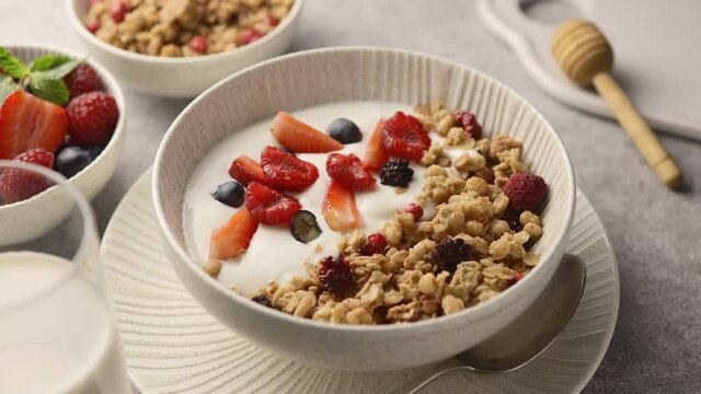 The camera pans over a plate of granola, berries and Greek yogurt. Decor from berries and honey, light background, close-up