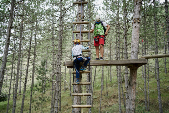 Unrecognizable Kid Climbing Ladder Near Male Instructor Standing On Platform While Spending Time In Adventure Park Together