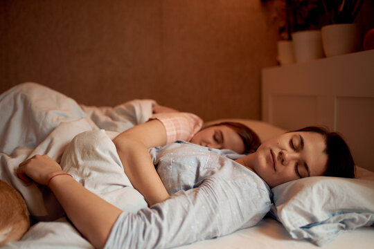 Loving couple of lesbian females lying in bed under blanket while sleeping in morning at home