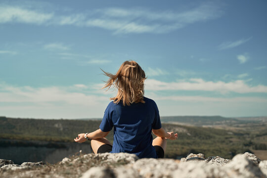 Back view of unrecognizable female traveler sitting in Lotus pose on hill and meditating with mudra hands while doing yoga in highlands during vacation