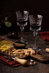 Cheese platter with different cheeses, sliced pear, nuts, honey and glasses of red wine on rustic wooden background. Retro styled cheese variety selection on wood board. Selective focus.