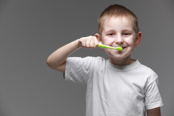 Happy child kid boy brushing teeth with toothbrush on gray background. Health care, dental hygiene. Mockup, copy space