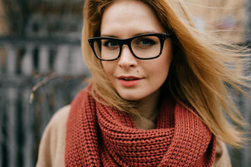 Portrait of young elegant blond girl with glasses and scarf posing outdoors