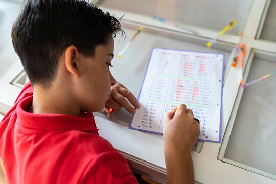 From above of crop anonymous boy in red polo shirt doing homework assignment with colorful pens and markers while sitting at wooden table