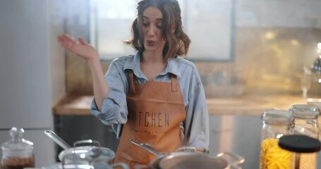 Tired and sad housewife standing hopelessly in a smoky kitchen from burnt food. Exhaustion from household chores and home routine concept