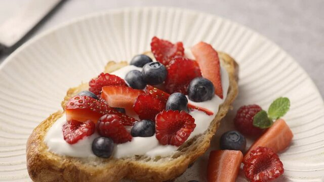 The camera pans over a croissant filled with berries and Greek yogurt. Farm berries decor, light background, close-up