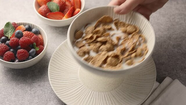The girl sets and clears a plate of multigrain breakfast cereals and milk. Decorated with berries, light colors 