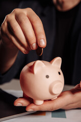 Man putting coin in pink piggy bank close-up. Saving money concept.