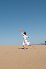 Fototapeta na wymiar woman dressed in white enjoying in the sand dunes on the sunny day