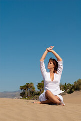 woman dressed in white performing meditation and yoga postures on the sand dunes on sunny day
