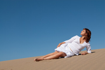 Fototapeta na wymiar woman dressed in white enjoying in the sand dunes on the sunny day