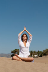 woman dressed in white performing meditation and yoga postures on the sand dunes on sunny day